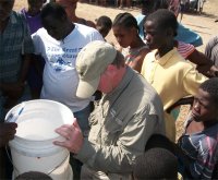 Dave Kanaga, head of the GAIN water project in Haiti praying over a water filter during a GAIN distribution of the Sawyer PointOne Water Filters in a tent city in Haiti